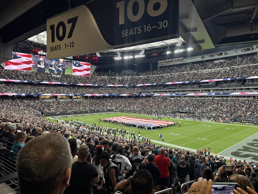 A crowd at a football stadium with a large United States flag spread across the field.
