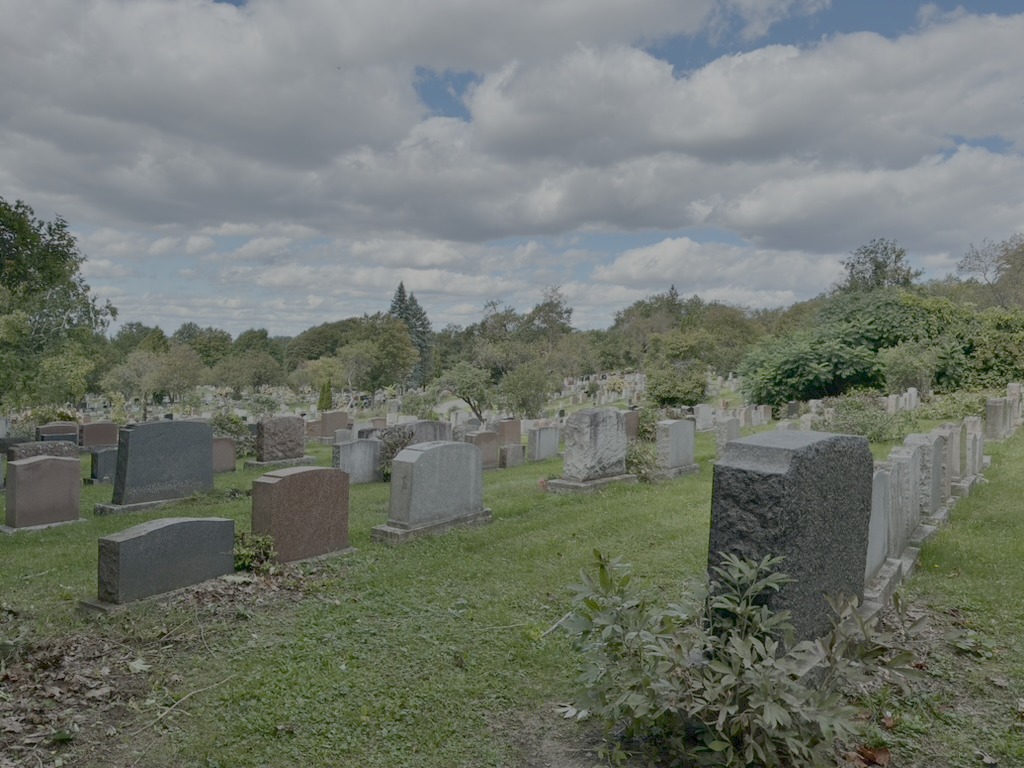 Gravestones across a green meadow beneath a cloudy sky