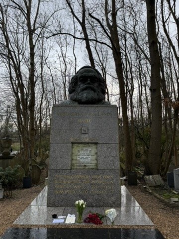 A stone memorial topped by a bearded bust, with flowers at its base